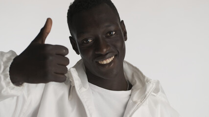 Attractive African American man dressed in casual wear keeping thumb up looking happy over white background. Like it expression
