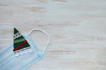 Medical protective mask with felt brooch in the shape of a Christmas tree on a white wooden...
