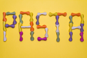 Colorful pasta sign made of raw pasta isolated on a yellow bristol background. Typography concept