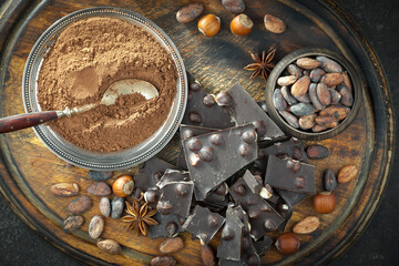 Dark chocolate in a composition with cocoa beans and nuts, on an old background.