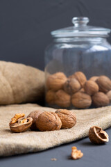 walnuts. unpeeled and peeled walnuts in shells on a black table and in a glass jar. brown nuts with sackcloth on a dark background. copy space. dried walnut and fruit. vertical