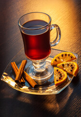 Tea in a glass cup on a saucer next to orange slices with cloves and cinnamon sticks. Wooden table...