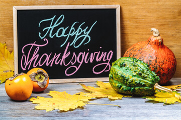 pumpkin, persimmon and autumn leaves on happy thanksgiving day lettering background