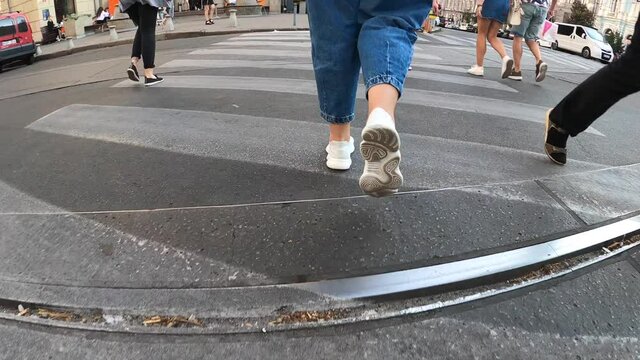 People crossing urban road through zebra, bottom view of woman legs in trainers