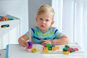 Little boy 2 years old is played with a wooden pyramid. Educational logic toys for children. Montessori games for child development.