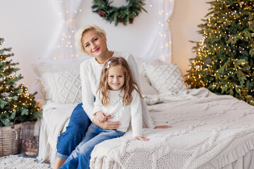 Mother and her daughter hugs in bed. Morning Christmas calmness relax cozy. New Year's decor in the bedroom. Xmas mood. Weekend leisure togetherness. Motherhood childhood. white sweater. Family 