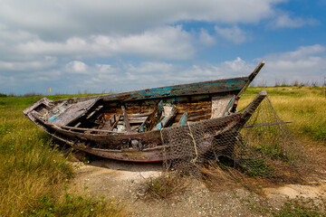 Abandoned fishing wooden boat with a net on the field