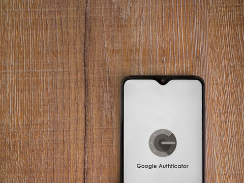 Lod, Israel - July 8, 2020: Google Authenticator app launch screen with logo on the display of a black mobile smartphone on wooden background. Top view flat lay with copy space.