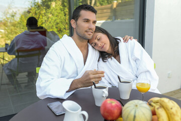 Happy young couple in bathrobes having breakfast outdoors