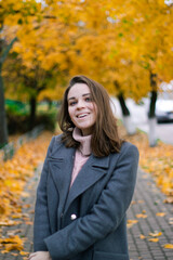 beautiful girl in an autumn coat walks in the park with autumn trees with yellowed leaves