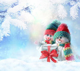 Two funny snowman with gift box in winter on the snow.