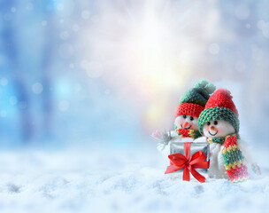 Two funny snowman with gift box in winter on the snow.