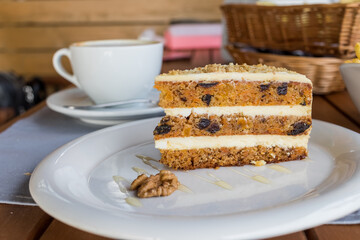 carrots and pumpkin cake with coffee cream in a cut on the plate.Delicious sliced carrot cake.Cup of cappuccino and Slice of cake on a white saucer, decorated with walnuts. dessert on plate