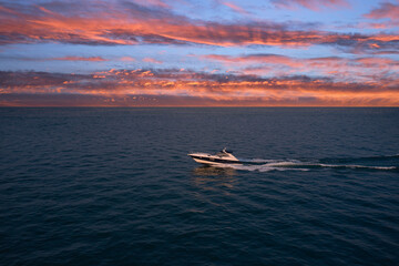 Side view of a modern speedboat in motion on the sea against the background of pink clouds at sunset. The yacht is moving fast at sunset.