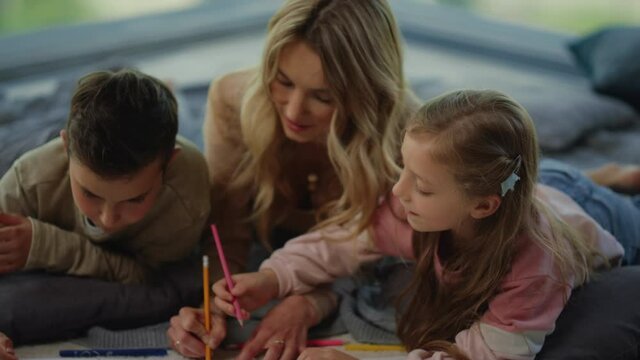 Young mother and kids drawing picture indoors. Family enjoying home time.