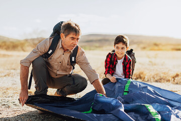 Grandfather and grandson setting up camping tent. Concept of elderly people with active life.