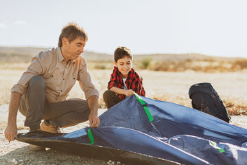 Grandfather and grandson setting up camping tent. Concept of elderly people with active life.