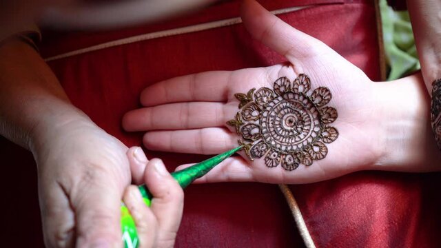 Top down flatlay shot of mehendi henna tattoo being applied on the hand of a woman for the hindu festival of karwachauth diwali dussera shaadi marriage and more shot in natural light on a red