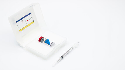 Vial of the COVID-19 vaccine inside its box with a syringe on white background