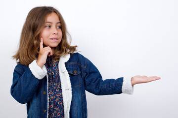 Funny Little caucasian girl with beautiful blue eyes wearing denim jacket standing over isolated white background holding open palm new product. I wanna buy it!