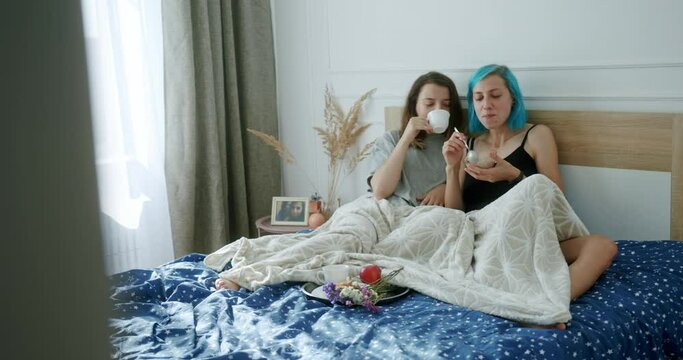 Two modern young woman in a same sex relationship sharing breakfast in bed viewed through an open door