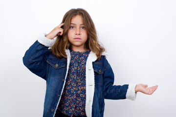 Little caucasian girl with beautiful blue eyes wearing denim jacket standing over isolated white confused and annoyed with open palm showing copy space and pointing finger to forehead. Think about it.