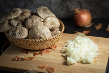Closeup of fresh white mushrooms in a basket with chopped onions on a cutting board