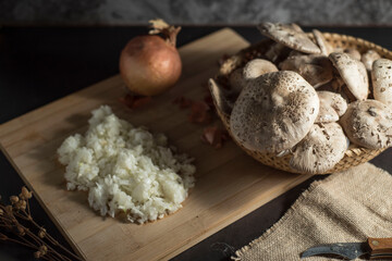 Closeup of fresh white mushrooms in a basket with chopped onions on a cutting board