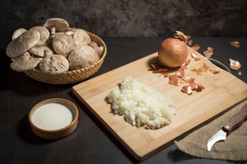 Closeup of fresh white mushrooms in a basket with chopped onions on a cutting board