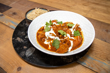 A plate delicious Butter Chilli chicken with rice on a wooden kitchen work top.