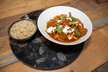 A plate delicious Butter Chilli chicken with rice on a wooden kitchen work top.