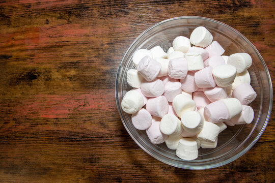 A bowl of delicious white and pink marshmallows on a brown wooden table