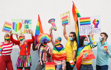 Gay people dance at pride parade with LGBT flags and banners while wearing protective face mask -...
