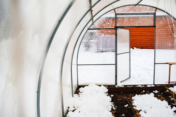 Polycarbonate greenhouse at the end of winter.Snow scattered in the greenhouse to moisten the soil. 