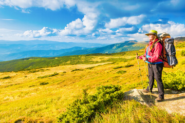 Obraz premium Happy traveling woman with backpack looking at mountain landscape
