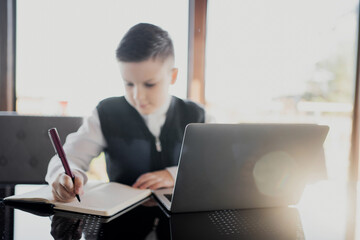 makes lessons online with a teacher and writes them in a notebook. dressed in a school white shirt and a stylish hairstyle studying on a laptop looking at the screen