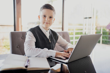 European appearance schoolboy boy dressed in a white shirt, looking at the camera. learning at home online on a laptop video call with an English teacher.