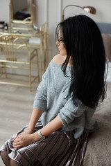 Young woman with dark hair and in round glasses posing at the dressing table in luxury interior