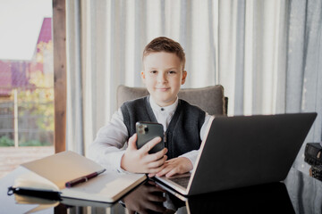 Fototapeta na wymiar does lessons online with a teacher. schoolboy boy dark-haired European appearance. dressed in a school white shirt and stylish hairstyle holding a laptop.