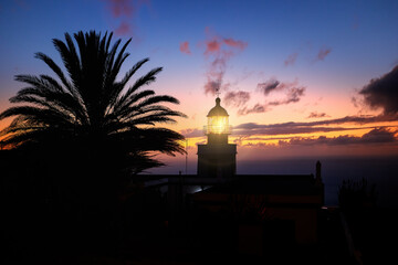 Ponta do Pargo lighthouse, silhouette of a glowing lighthouse against an orange evening sky. Tourist place. Traveling around Madeira island, Portugal