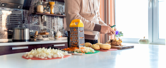 Cooking man, father, cooker. Preparation of soup, lunch, dinner in kitchen. Cutting vegetables, potatoes, carrots, onions on wooden board.Large knife.Large pot of boiling water.Surprise,help for wife