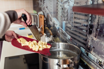 Cooking man, father, cooker. Preparation of soup, lunch, dinner in kitchen. Cutting vegetables, potatoes, carrots, onions on wooden board.Large knife.Large pot of boiling water.Surprise,help for wife