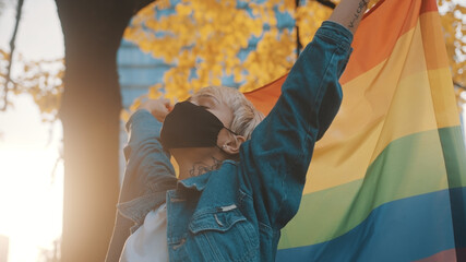 Proud young blond woman with face mask waving rainbow flag. Close up. High quality photo