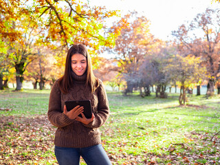 Young pretty woman smiling with tablet in an oak forest in autumn.