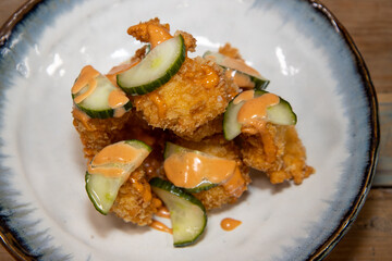 A delicious plate of fried chicken with chilli mayonnaise mayo and cucumber slices on a wooden kitchen work top