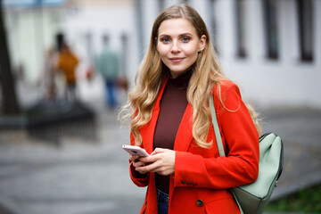 Cheerful young woman wearing coat walking with smartphone