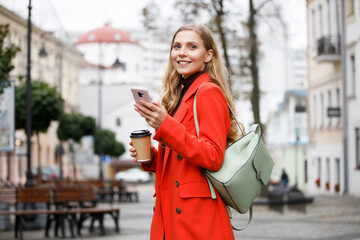 Attractive young woman wearing coat walking with coffee cup and cellphone