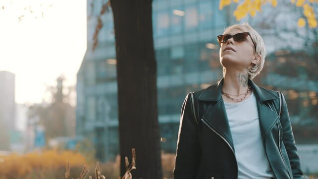 Young woman with blond short hair and sunglasses posing in park with hands over the head. High quality 4k footage