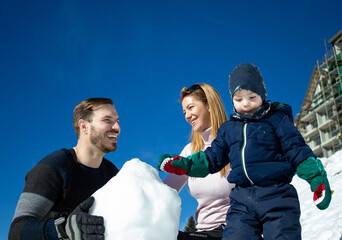 Obraz premium Parents with boy making snowman on mountain