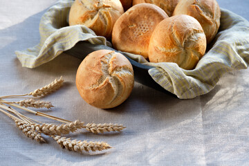 Kaiser or Vienna rolls on baking paper. Table covered with beige linen tablecloth.